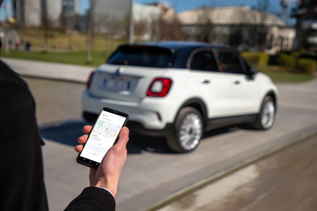 Person mit Smartphone und Standortanzeige in der Fiat-App vor dem Auto