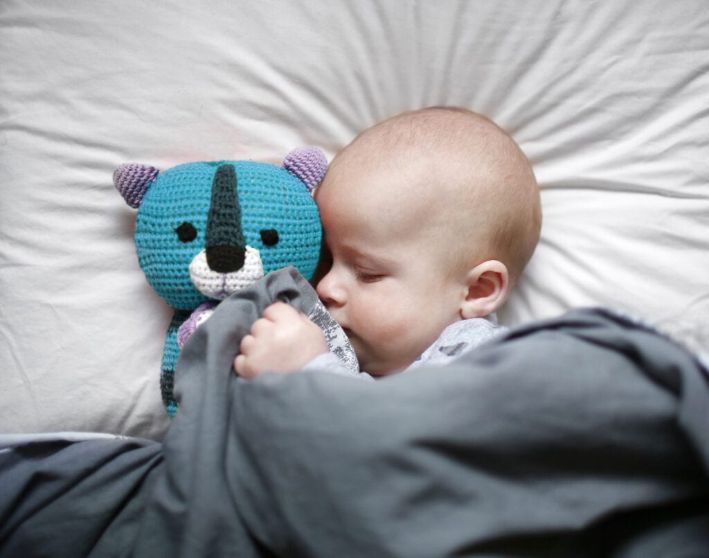 Schlafendes Baby mit Kuscheltier in Bett