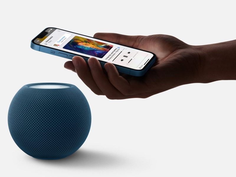 Eine Hand hält ein Smartphone vor einen HomePod mini