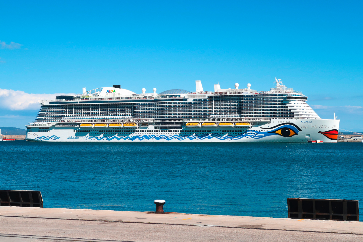 Von Hafenkante Blick auf blaues Wasser mit großem AIDA-Schiff am Horizont