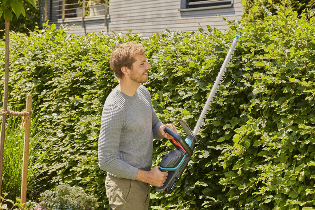 Mann stutzt mit Heckenschere eine Hecke.