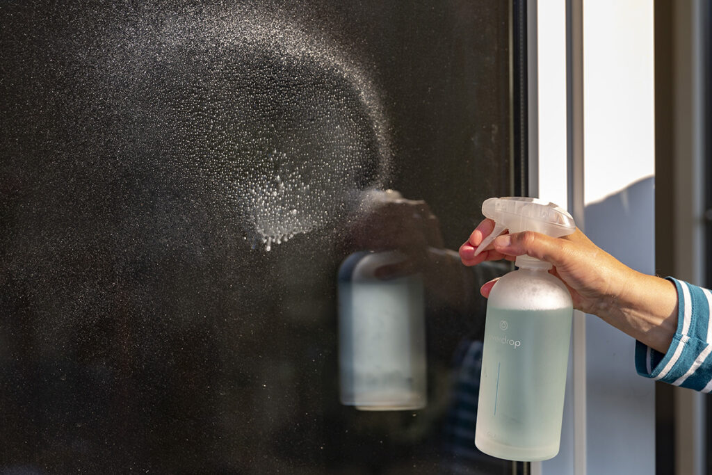 Hand mit Sprühflasche sprüht Glasscheibe ein