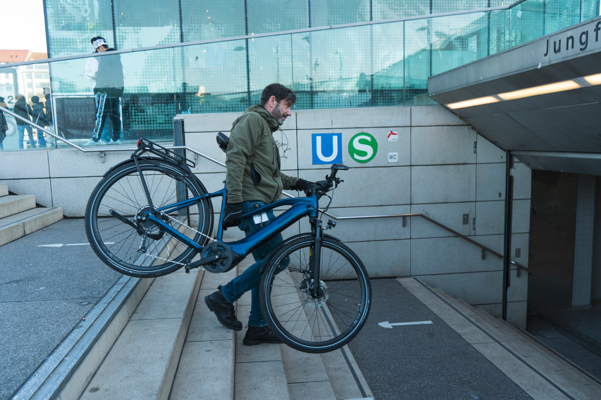 Mann trägt Trekking-E-Bike Aufgang zur U-Bahn hinunter