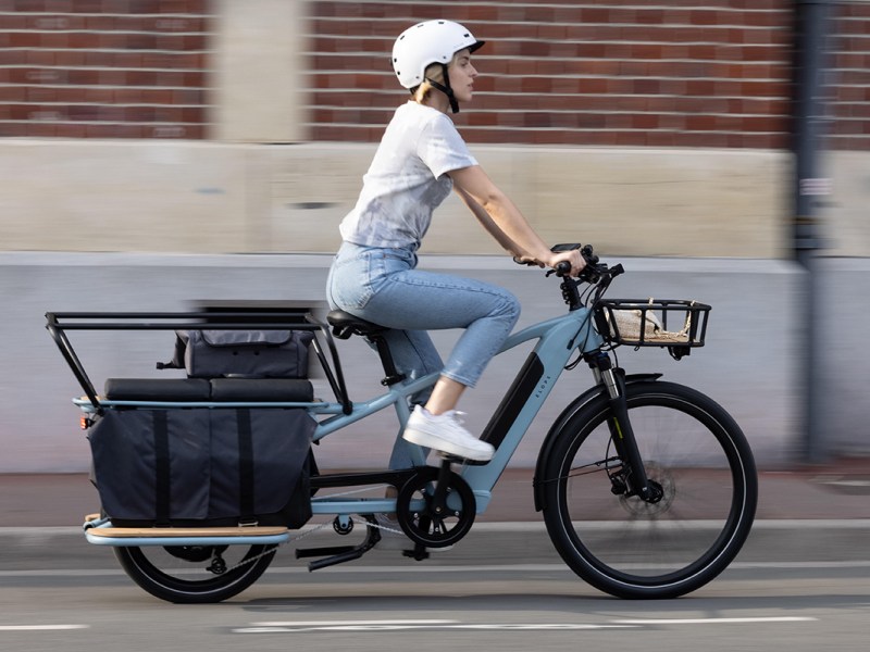 Das E-Lastenfahrrad R500E Langtail von Decatholn in Fahrt: Eine junge Frau ist damit in der Stadt unterwegs.