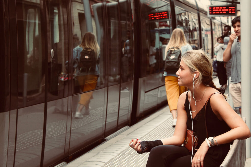 Eine junge Frau sitzt an einem Bahnsteig und wartet auf eine Bahn.
