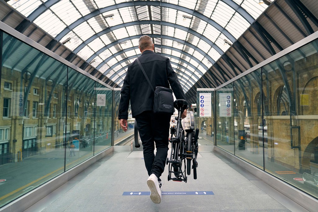 Mann trägt zusammengeklapptes E-Faltrad durch Bahnhofshalle