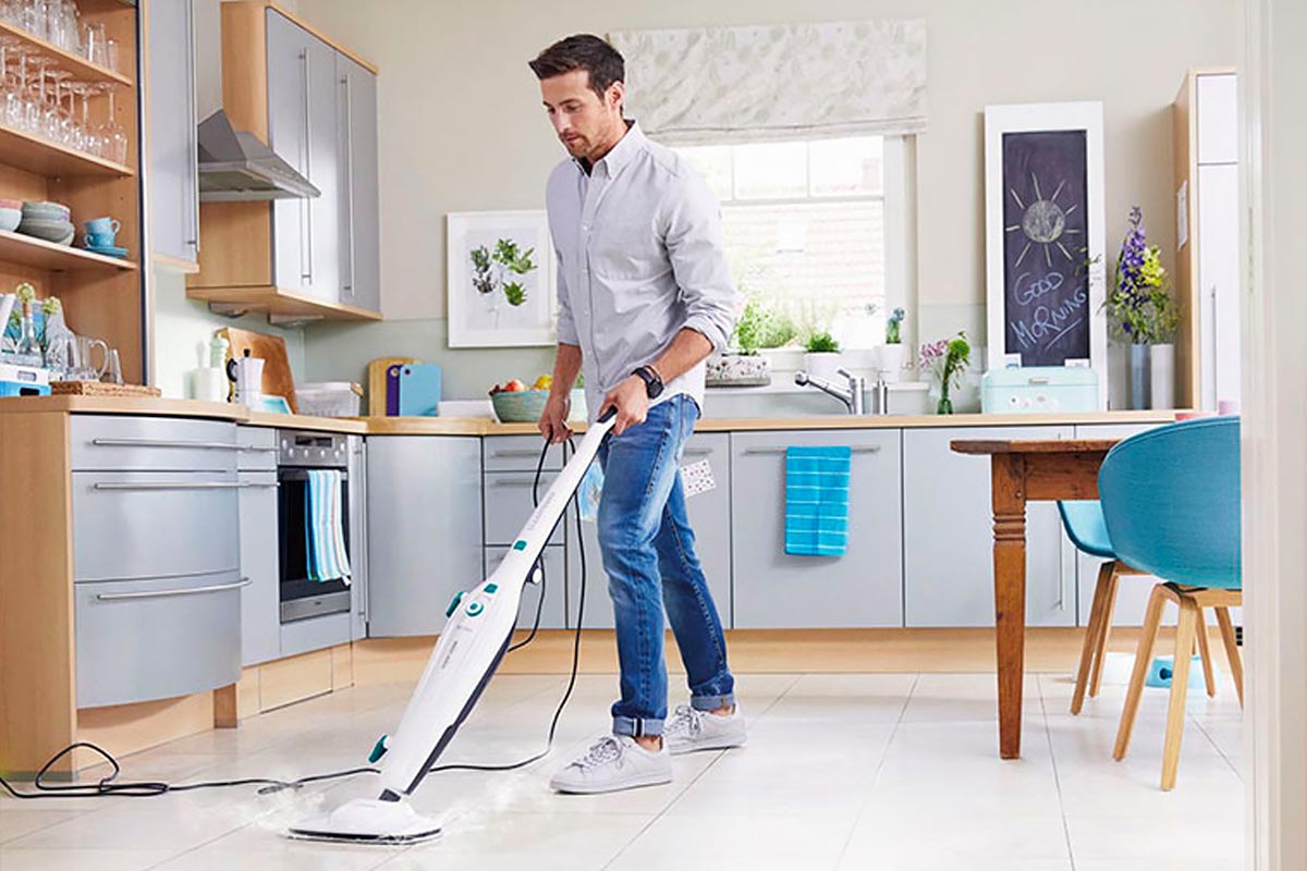 Ein Mann in einer Küche säubert den Boden mit dem Clean Tenso Power Dampfreiniger von Leifheit.