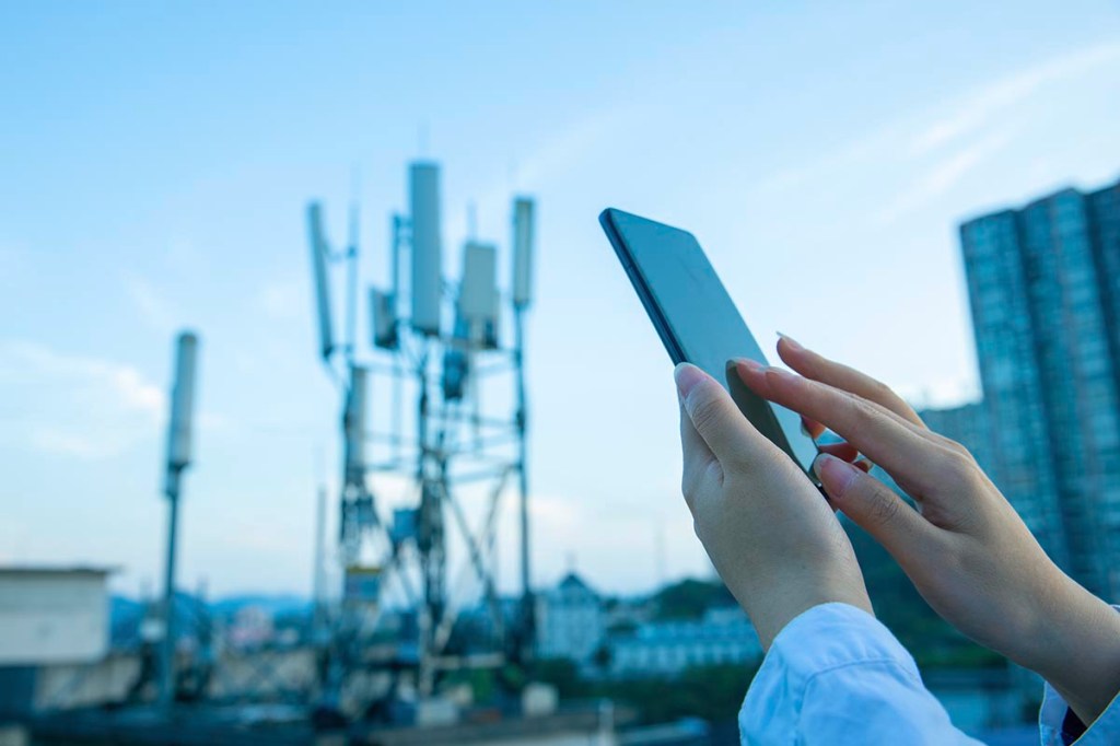 Hand mit Smartphone vor einem 5G-Mast