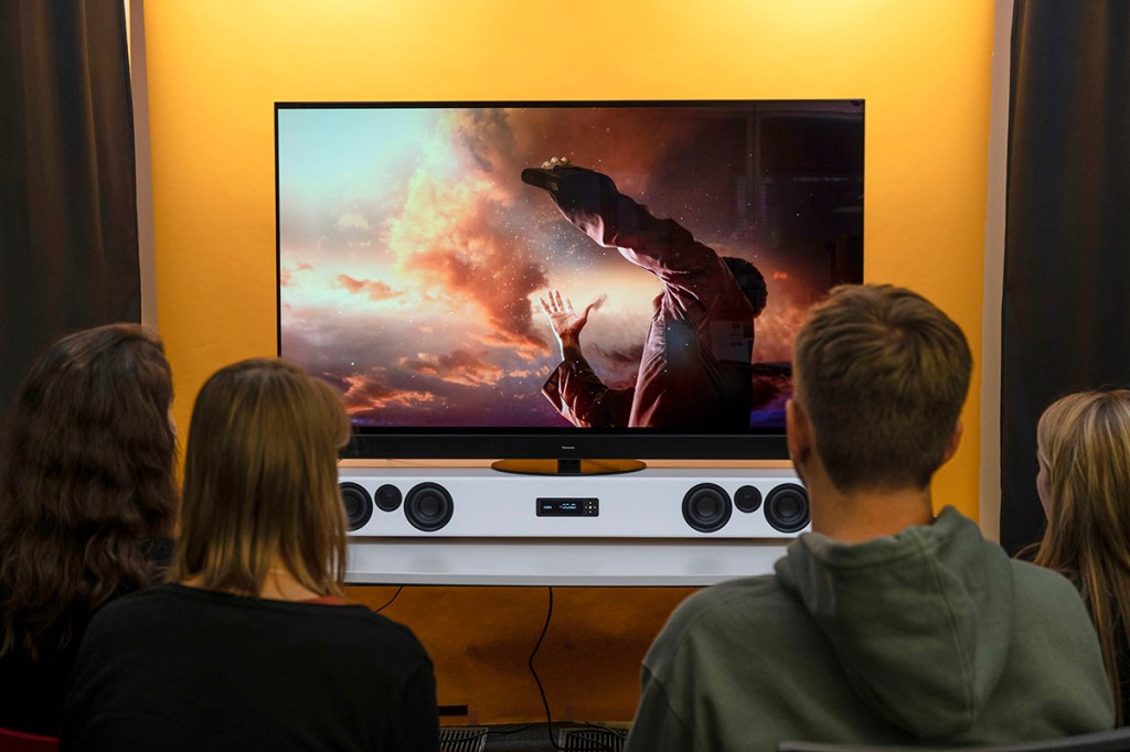 Vier Personen sitzen vor einem TV-Gerät und lauschen den Klängen einer Soundbar.