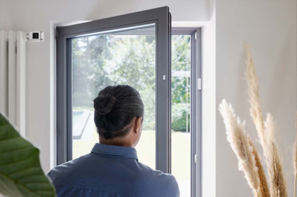 Person im Anschnitt von hinten, steht an einer geöffneten Fenstertür