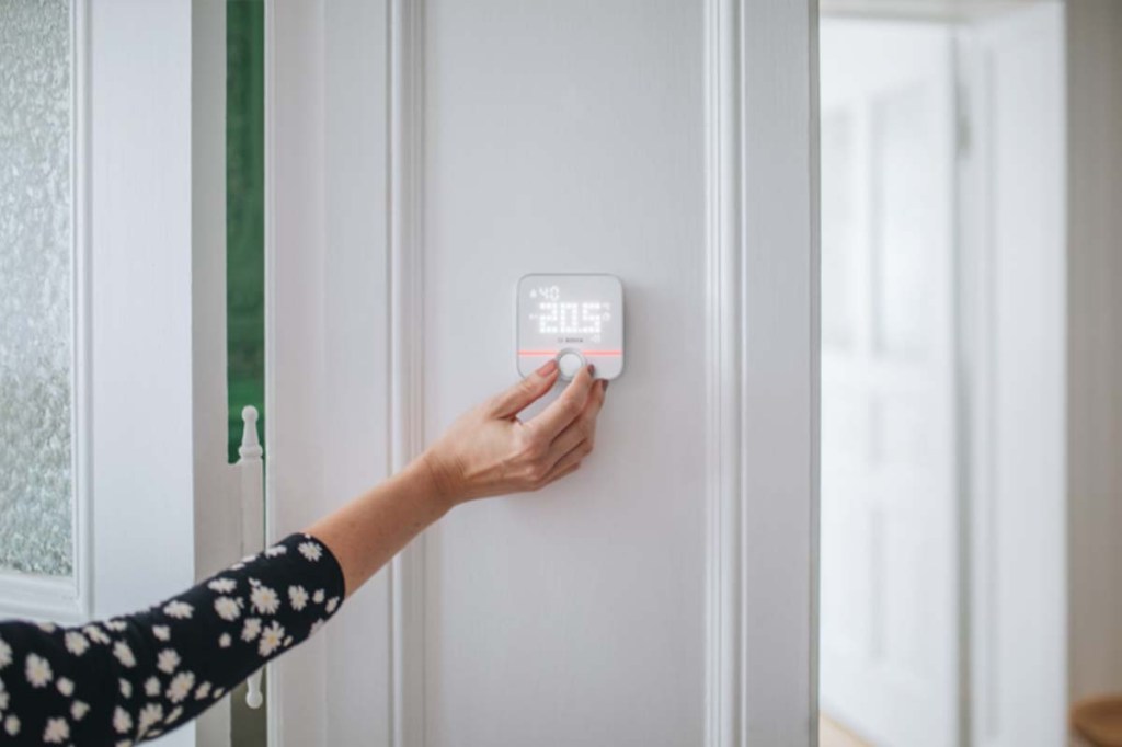 elektrisches Thermostat an einer Wand hängen, wird von einer Hand bedient