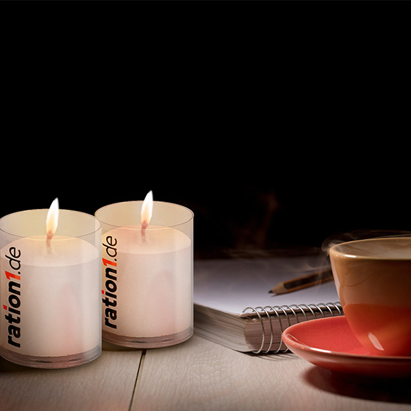 Zwei weiße brennende Kerzen neben Schreibblock und oranger Tasse vor dunklem Hintergrund