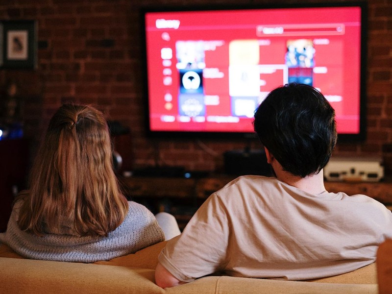 Zwei Personen auf einem Sofa schauen auf einen Fernseher