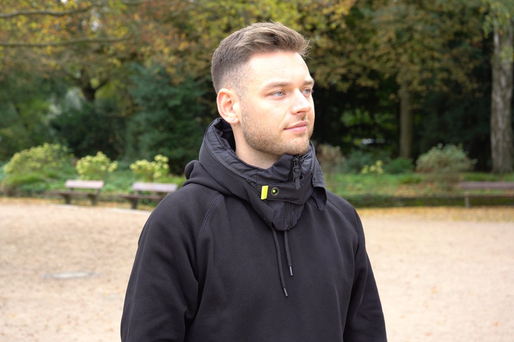 Mann mit Hövding Helm um den Hals im Park stehend