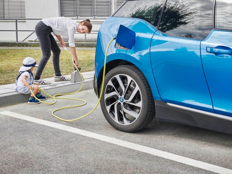 An einem E-Auto-Ladepunkt ist ein blaues Auto angeschlossen.