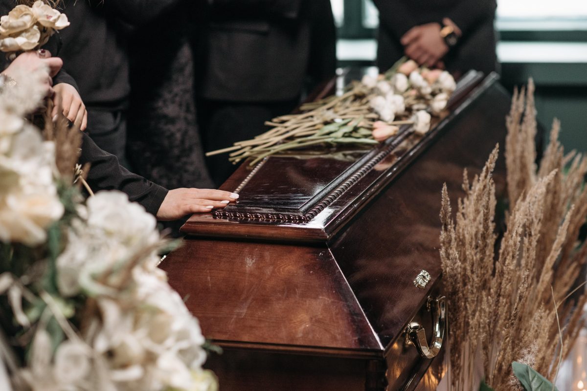 Personen stehen um einen Sarg herum, der mit Blumen geschmückt ist.