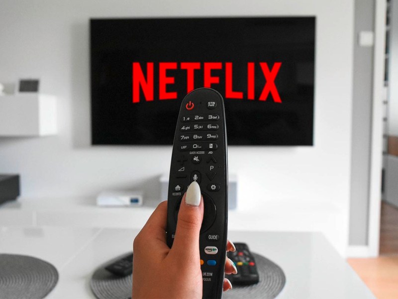 Hand mit Fernbedienung vor Bildschirm mit Logo von Netflix