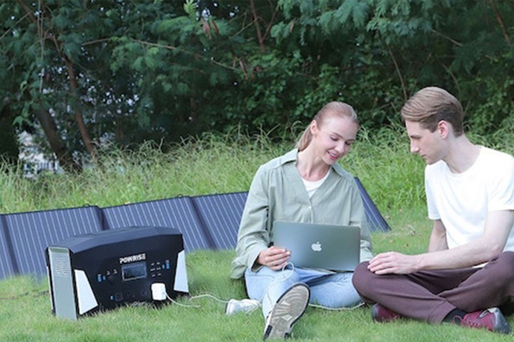 Zwei Personen sitzen auf einer Wiese und laden die Powrise 2200 mit einem Solarpanel.