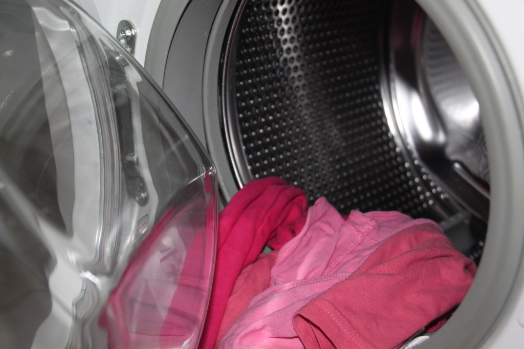 Einige Wäschestücke hängen aus einer leeren Trockner-Trommel.