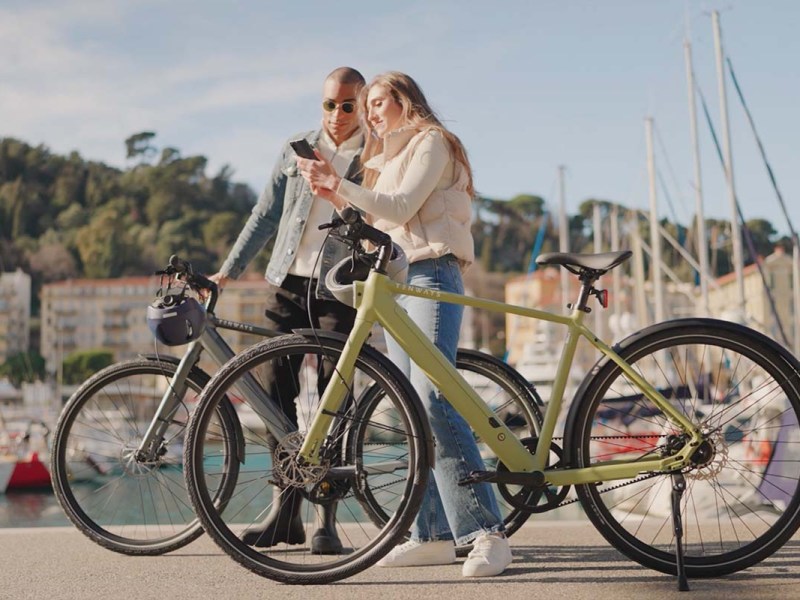 zwei Menschen stehen neben ihren E-Bikes CGOP600 Pro von Tenways und gucken zusammen auf ein Handy, ein Hafen im HIntergrund