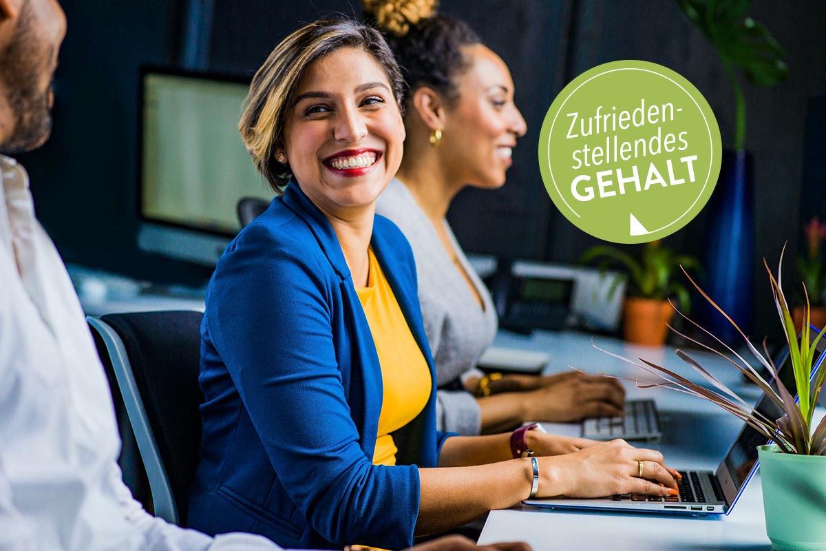 Zwei lächelnde Frauen am Arbeitsplatz vor einem Laptop