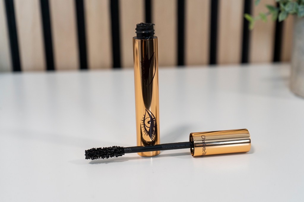 Geöffnete Mascara Flasche mit Bürste vorne auf weißem Tisch liegend, golden