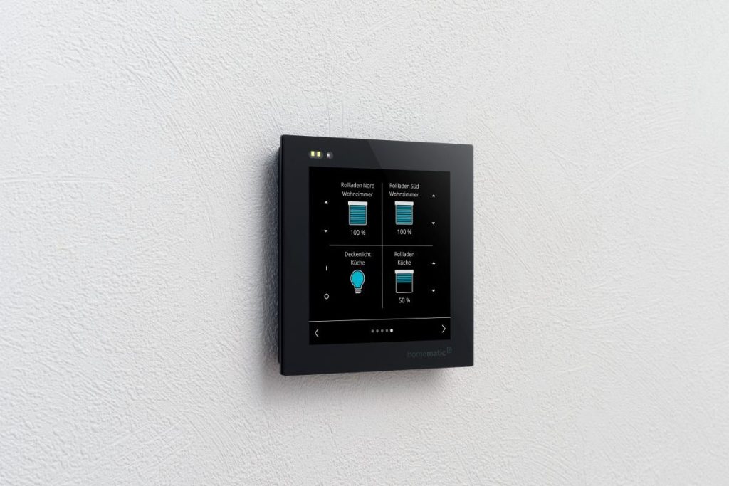 Ein Homematic IP Wired Glasdisplay hängt an einer Wand und zeigt vier verschiedene Kacheln.