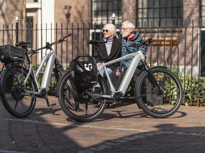 Zwei ältere Menschen sitzen auf einer Bank, vor ihnen stehen ihre E-Bikes