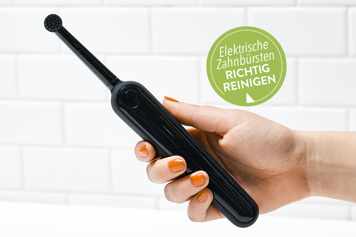 Hand mit roten Fingernägeln hält schwarze elektrische Zahnbürste vor weißer Steinwand; grüner Button oben rechts "Elektrische Zahnbürste richtig reinigen"