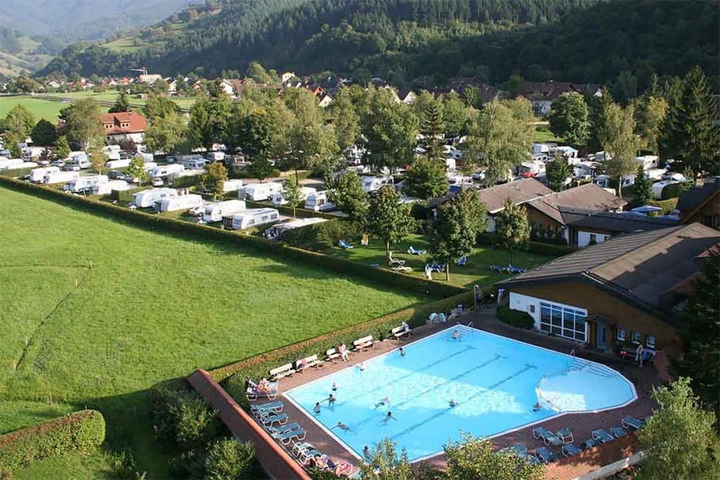 Pool neben wiese und Campingplatz mit weißen Wohnmobilen und Bäumen von oben