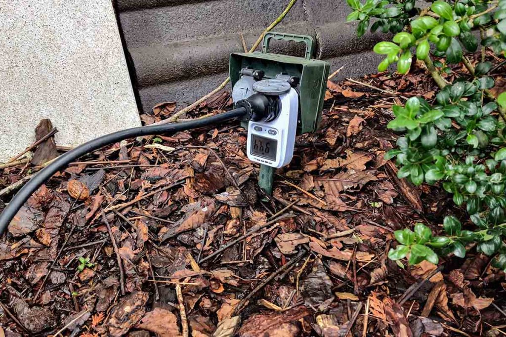 Der Stecker des freistehenden Balkonkraftwerks in der Außensteckdose mit Messgerät.