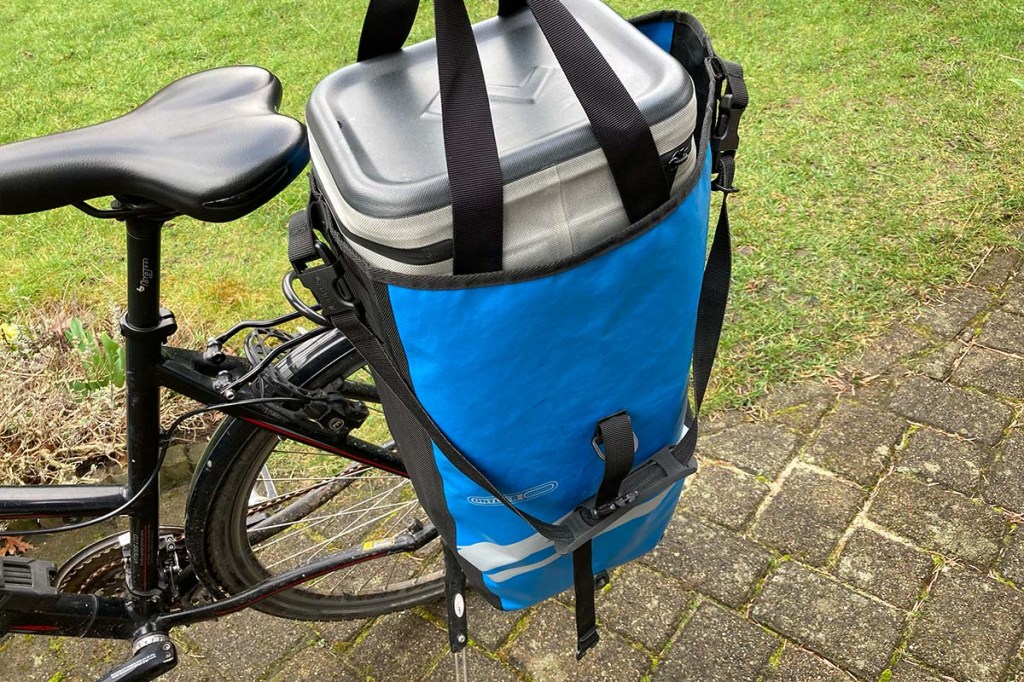 Nahaufnahme HInterteil eines Fahrrads, an dem eine Tasche hängt, Kühltasche guckt aus der Tasche raus