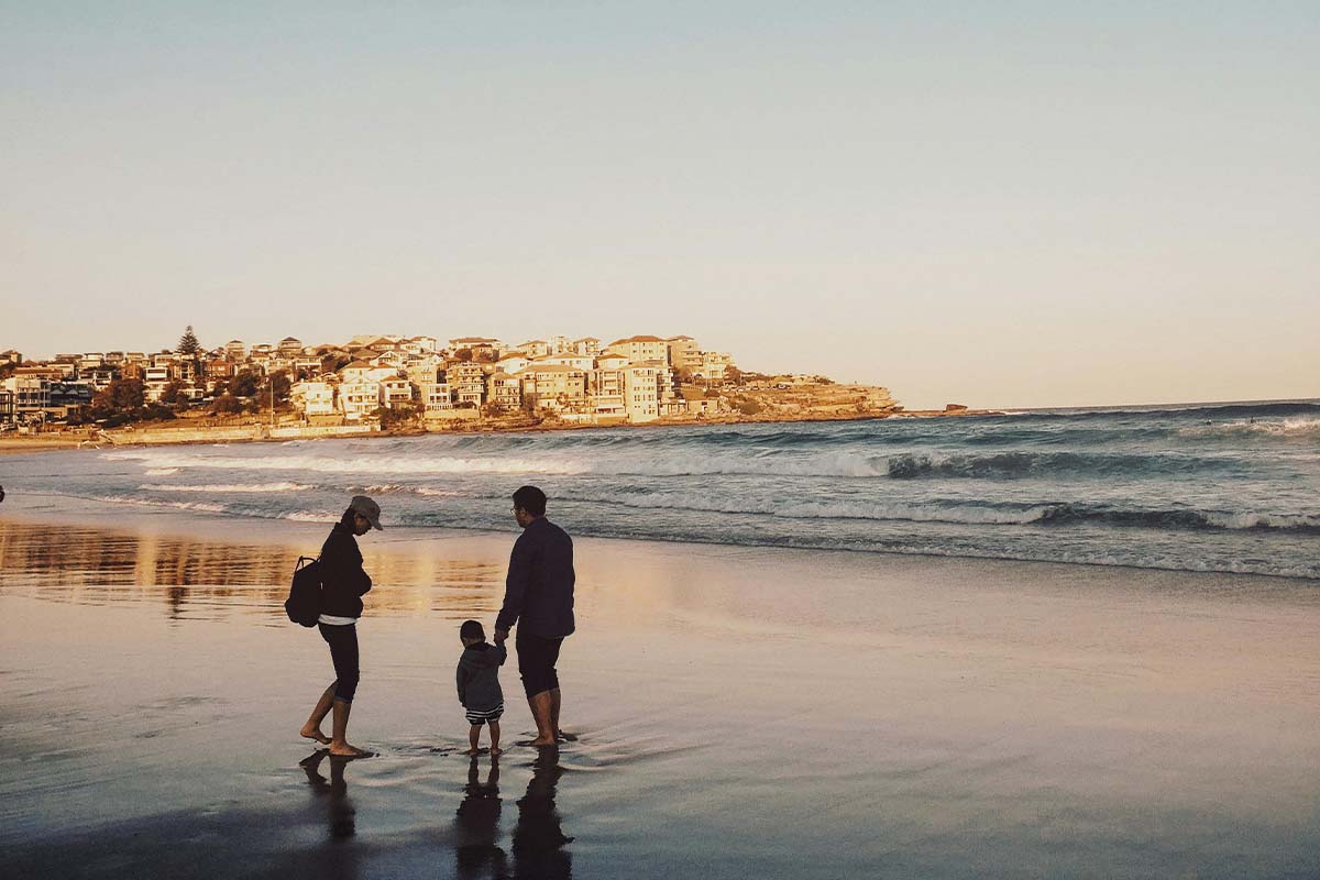 familie bei sonnenuntergang an einem Strand, im Hintergrund sieht man einen Küstenort