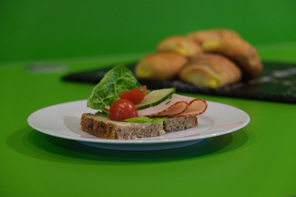 Belegtes Brot mit Tomate, Gurke und Salatblatt vor grüner Wand