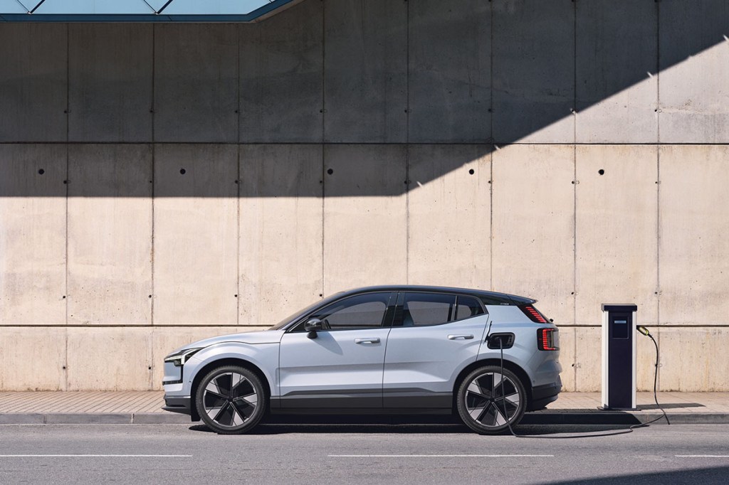 E-Auto Volvo EX30 steht auf einer Straße im Profil vor einer Ladesäule.