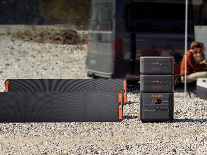 Die Jackery Explorer 2000 Plus mit zwei Zusatz-Akkus und Solarpanels vor einem Camping-Van.