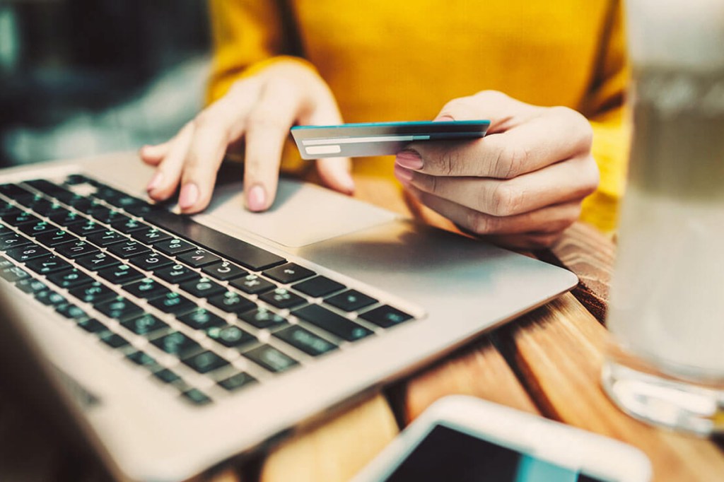 Eine Frau bedient ein Laptop und hält eine Bankkarte in der Hand.