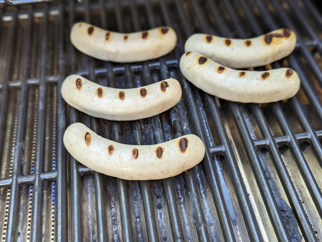 Fünf Bratwürste mit Röststreifen auf dem Rost des Char-Broil