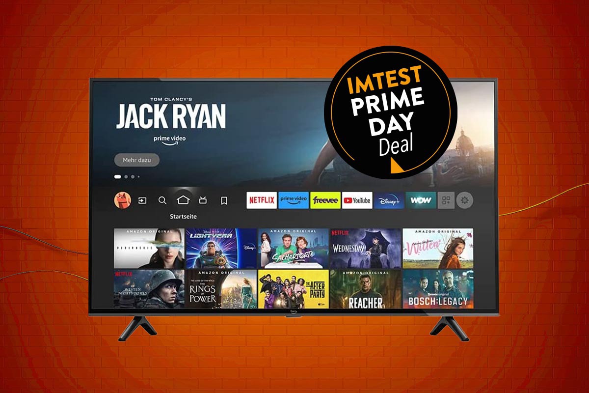 Amazon Fire TV Fernseher von vorne mit geöffneter Mediathek auf orangenem Hintergrund mit schwarzem Button "IMTEST Prime Day Deal"