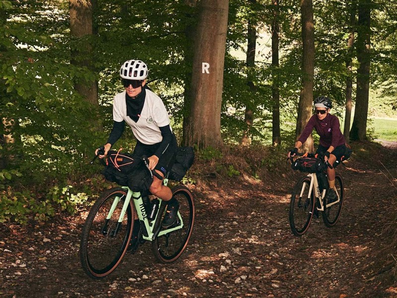 Zwei Personen fahren mit einem E-Gravelbike durch einen Wald