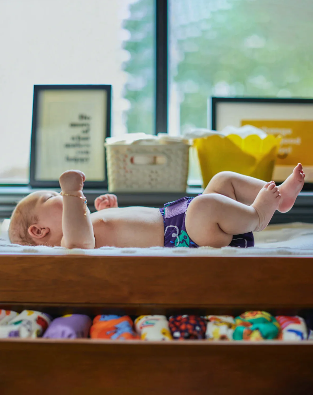 EinBaby in einem Holzbettchen und Mehrwegwindeln unter dem Bett.