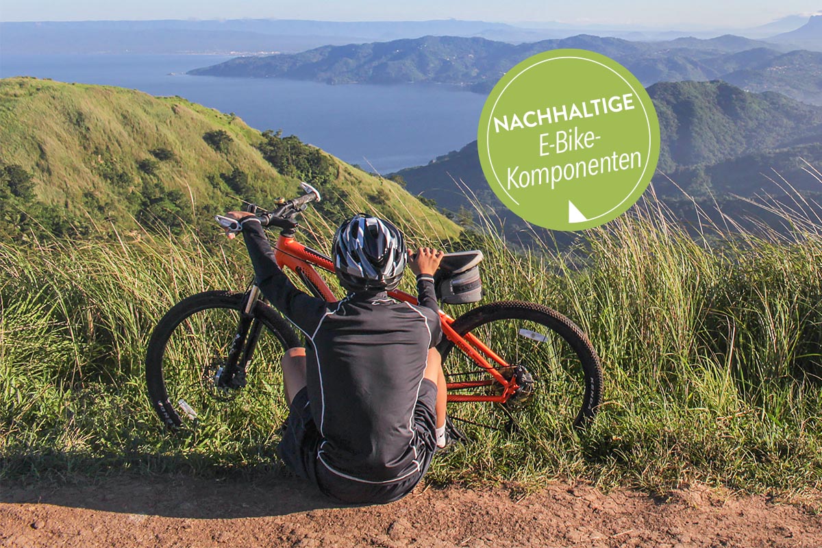 Mann sitzt vor seinem Fahrrad in der Natur, im Hintergrund ist ein See