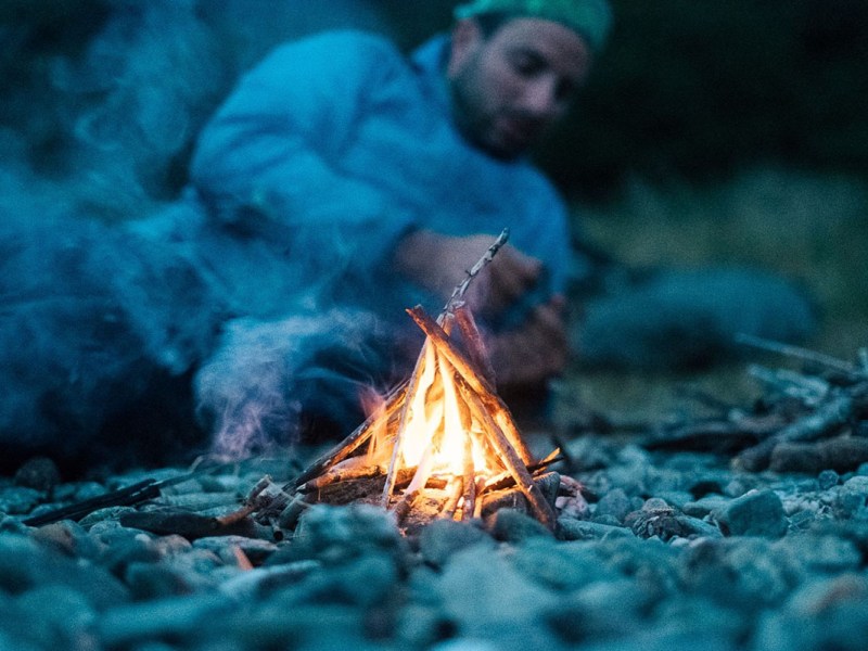 Ein Mann liegt an einem Lagerfeuer.