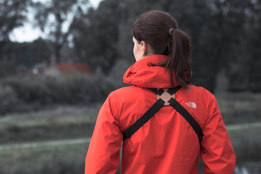 Frau mit roter Jacke trägt einen Fernglas-Kreuzgurt.