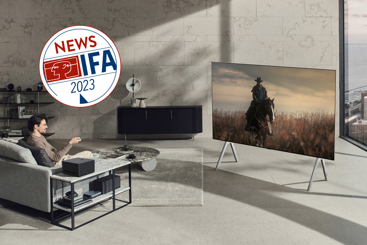 Ein großer Fernseher von LG steht in einem steinverkleideten Raum, davor ein Mensch auf einem grauen Sofa.