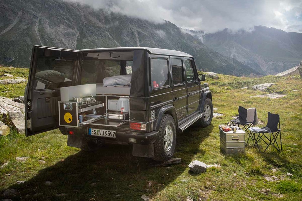 Ein Geländewagen vor Bergpanorama. Die Kofferraum-Tür ist geöffnet und darin steht eine QUQUQ-Campingbox.
