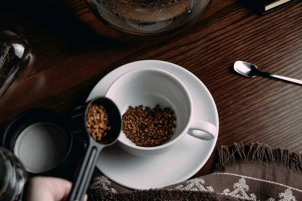 Löffel mit löslichem Kaffee über Kaffeetasse.