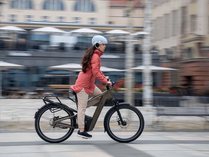 Frau fährt mit einem E-Bike durch eine städtische Gegend, der Hintergrund ist verschwommen