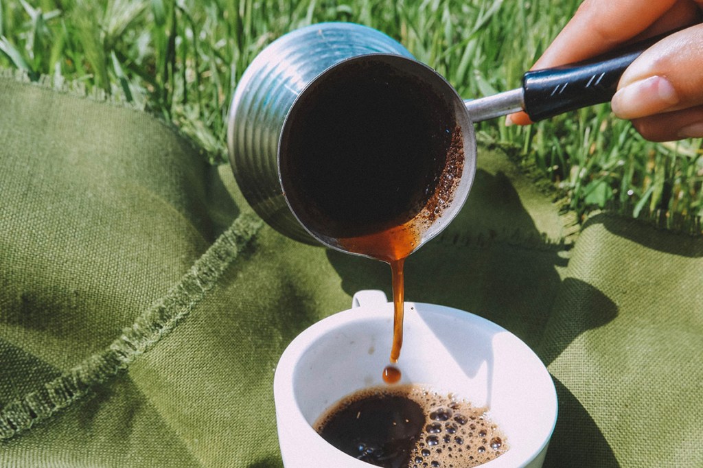 Kaffee wird aus einem Zubreiter für türkischen Kaffee in eine Tasse gegeossen.