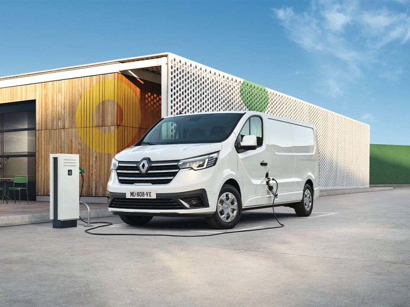 Grafik: Renault Trafic E-Tech Electric vor einer Lagerhalle, ist an einem Ladekabel angeschlossen